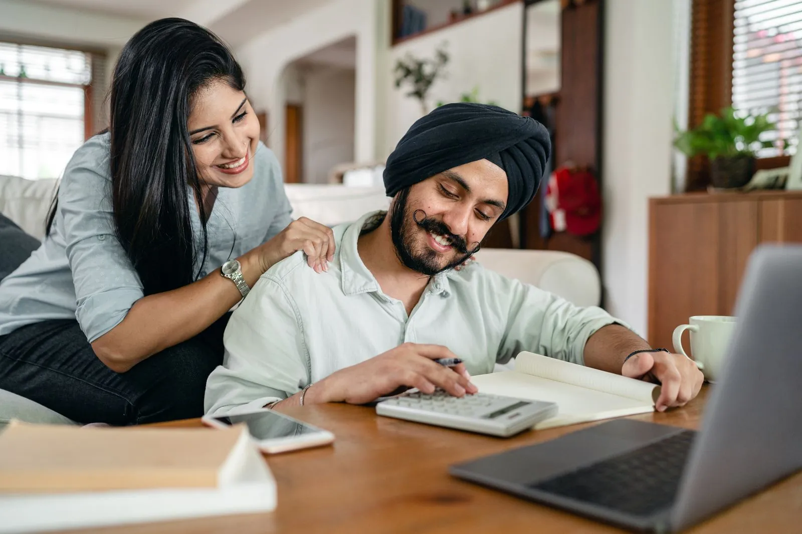 A couple reviews household finances at home with a calculator and laptop.