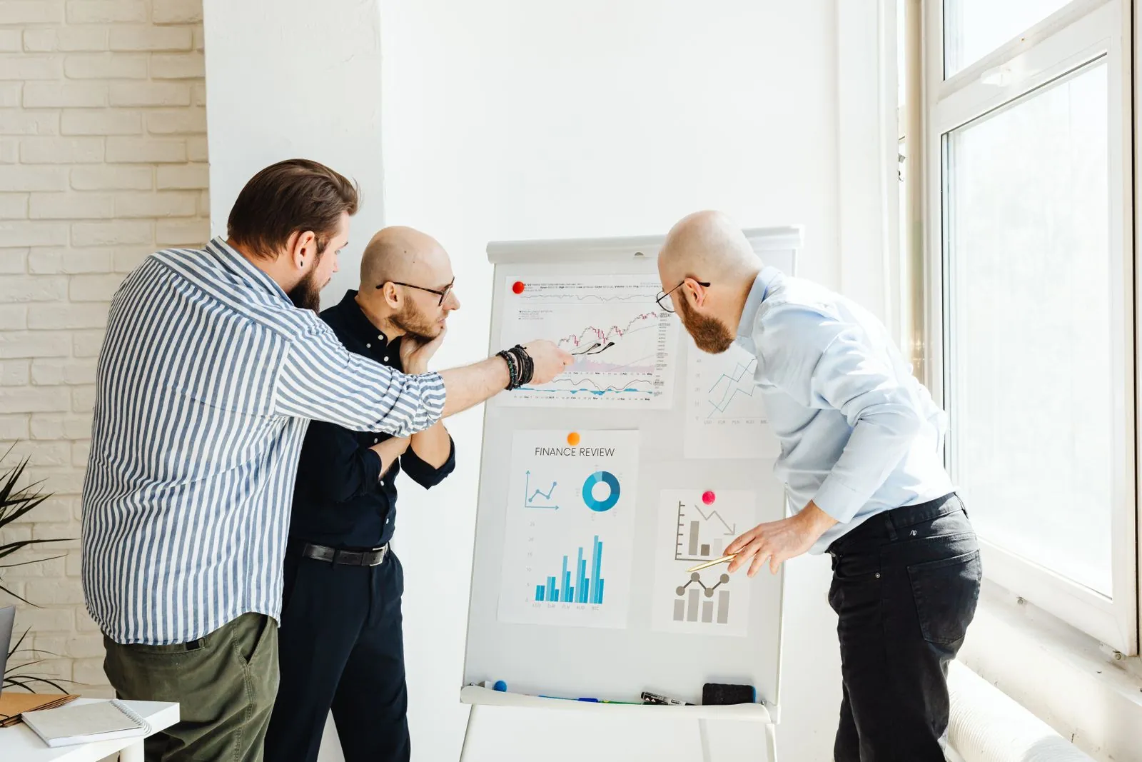Three colleagues discuss financial charts on a whiteboard.