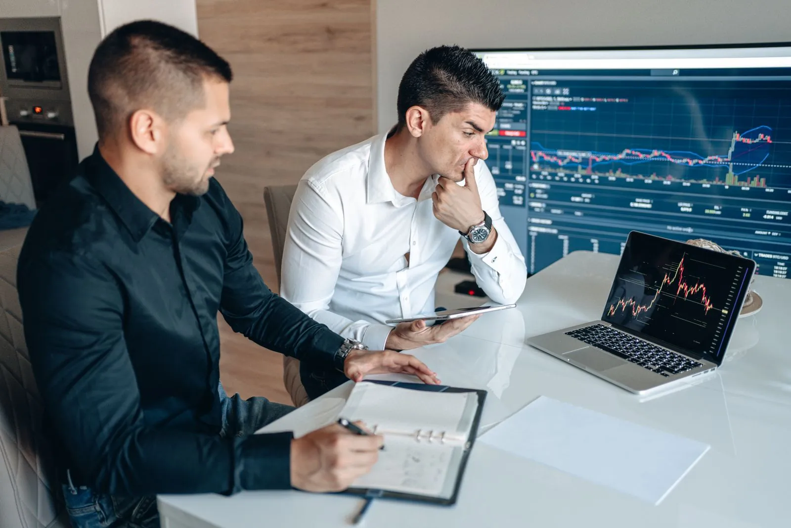 Two people compare investment charts at a desk.